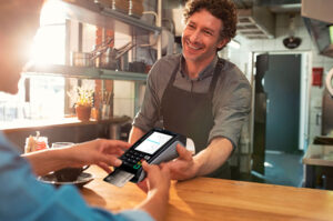 Customer paying as employee in an apron smiles holding the point of sale device